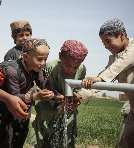 School-age children play with water from a pump.