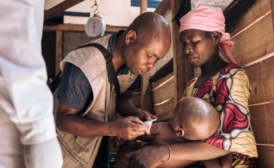A health worker checks the nutrition status of a young boy as his mother holds him.