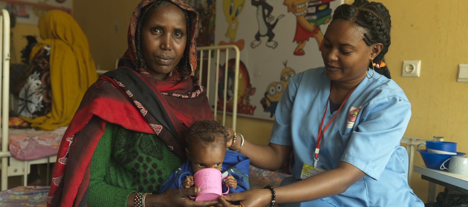 At the Stabilization Center at Yabelo General Hospital in Ethiopia, Nurse Ware helps severely malnourished Dabo drink therapeutic milk as treatment for Dabo's malnutrition.