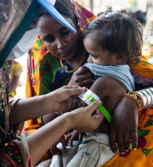 Samina (right), an Action Against Hunger Community Health Worker, checks 4-year-old Kailash's arm with a color-coded measuring tape to see if he has gained weight since her last visit.