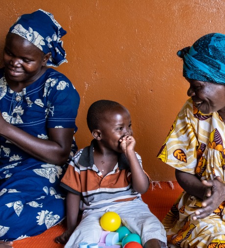 A child disabled by severe malnutrition at a young age is receiving motor skills training at the Rehabilitation center for the physically disabled (CRHAM) supported by ACF. Here, he is surrounded by the mother of another child like him and by his grandmother. Bangui, CAR. 2022