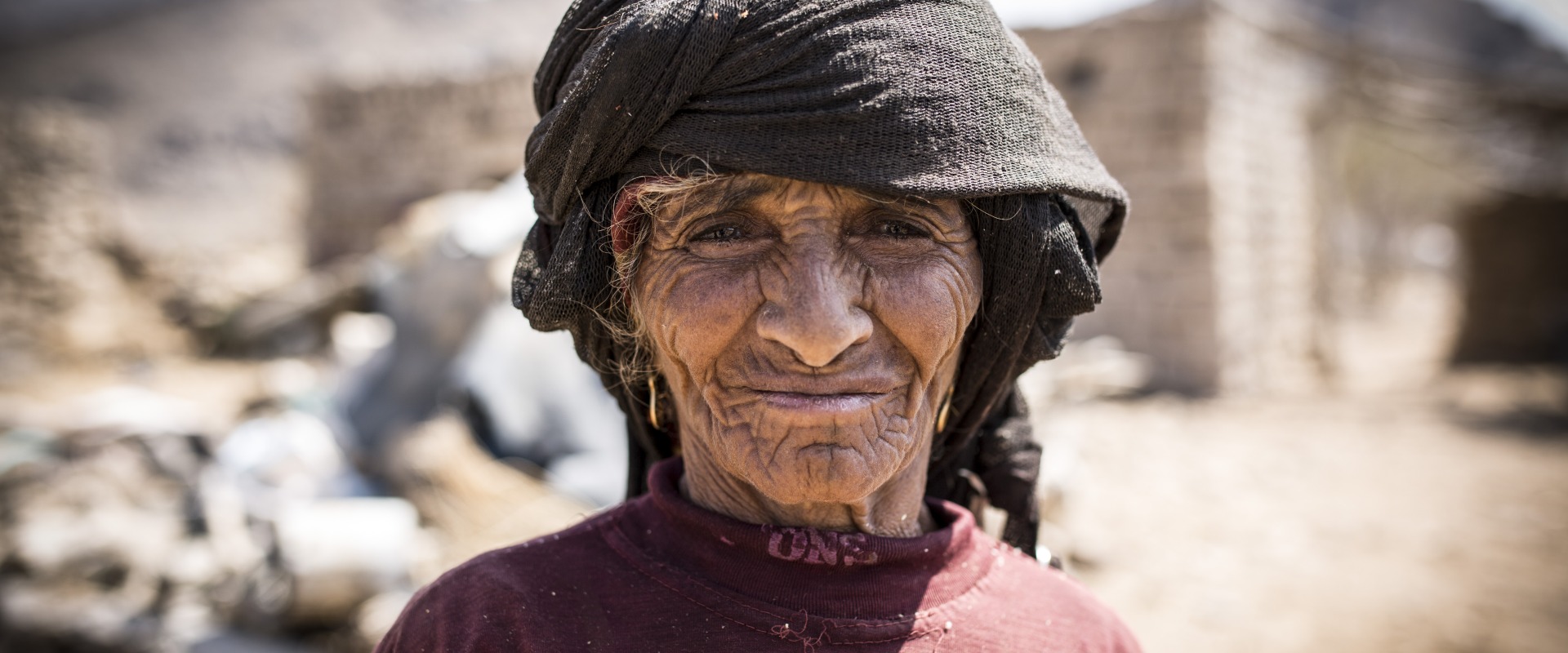 In Yemen, a woman stands in front of her community, which has been destroyed by conflict.